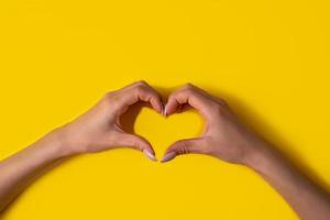 corazón haciendo manos de mujer con manicura sobre fondo amarillo, vista superior foto