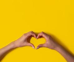 corazón haciendo manos de mujer con manicura sobre fondo amarillo, vista superior, pancarta foto