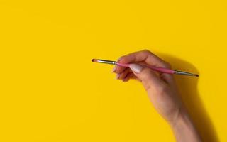 Female hand with a brush on a yellow background, top view photo
