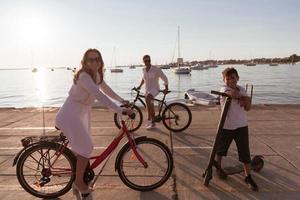 Happy family enjoying a beautiful morning by the sea together, parents riding a bike and their son riding an electric scooter. Selective focus photo