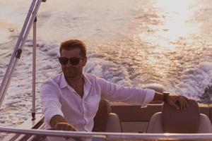 A determined senior businessman in casual clothes and sunglasses enjoys his vacation driving a luxury boat at sunset. Selective focus photo