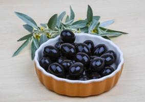 Black olives in a bowl on wooden background photo