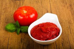 Tomato paste in a bowl on wooden background photo