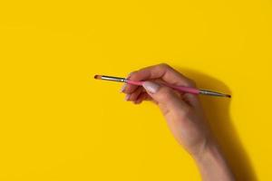 Female hand with a brush on a yellow background, top view photo