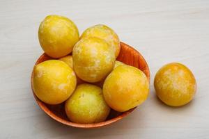 Yellow plums in a bowl on wooden background photo