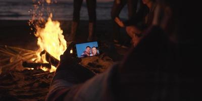 Couple taking photos beside campfire on beach