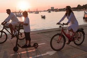 Happy family enjoying a beautiful morning by the sea together, parents riding a bike and their son riding an electric scooter. Selective focus photo