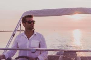 A determined senior businessman in casual clothes and sunglasses enjoys his vacation driving a luxury boat at sunset. Selective focus photo