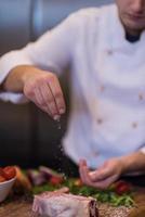 chef poniendo sal en una jugosa rebanada de bistec crudo foto