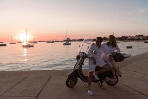 The couple enjoys a vacation while sitting on a scooter by the sea and enjoying the beautiful sunrise. Selective focus photo