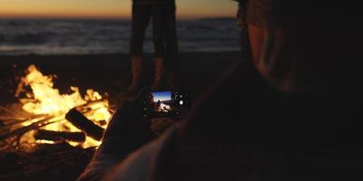 pareja tomando fotos junto a una fogata en la playa