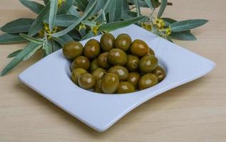 aceitunas verdes en un recipiente sobre fondo de madera foto