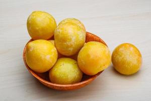 Yellow plums in a bowl on wooden background photo