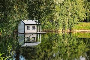 casa de pato flotante de madera blanca en el centro del estanque en un parque público. santuario de aves en lago artificial. nido de primavera. vista verde de verano. reserva natural de vida silvestre en el agua del río. refugio de aves acuáticas foto