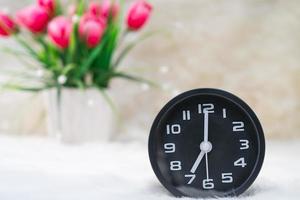 Black alarm clock and flower in vase on table photo