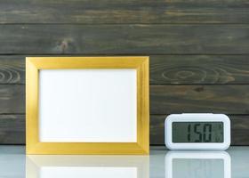 Blank golden frame and digital alarm clock on table photo