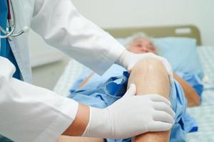 Doctor checking Asian elderly woman patient with scar knee replacement surgery in hospital. photo