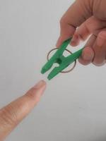 A hand tries to pinch his thumb using a green clothespin. photo