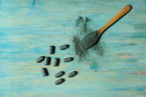 Pills of chlorella, spirulina, barley and powder in a wooden spoon on a blue wooden background. Nutritional supplement, detox superfood top view photo