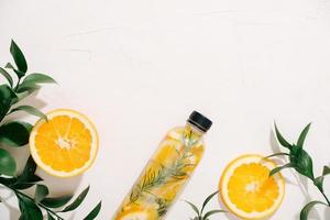 Leaves and bottle tropical water on white background. Detox fruit infused water, citrus fruits and rosemary leaves. Top view, flat lay, copy space photo