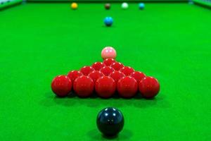 The snooker balls on the table consist of red, black, pink, blue, green, white, brown, and yellow, the focus is on the red ball. photo