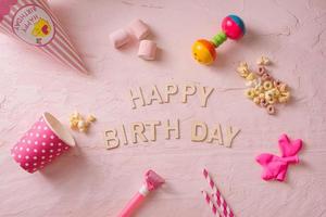 Birthday party background, border of confetti, sweets, lollipops and gift on pink surface, copy space, top view photo