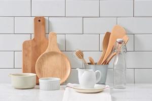 Simple rustic kitchenware against white wooden wall rough ceramic pot with wooden cooking utensil set, stacks of ceramic bowls, jug and wooden trays. photo