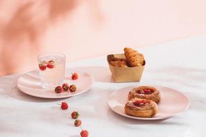 Sweet summer dessert, homemade baked mini croissants, served with cold raspberry cider, fresh raspberries. On a white marble table, copy space top view photo