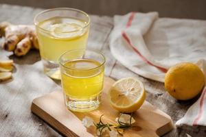 Refreshing summer drink with lemon, ginger, rosemary and ice on rustic wooden table, copy space photo