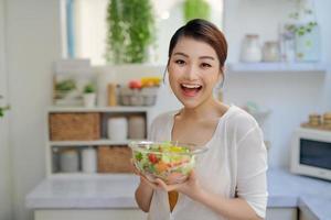 Young beautiful woman eating fresh salad at home photo