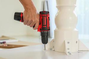 man assembling white table furniture at home using cordless screwdriver photo