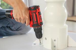 man assembling white table furniture at home using cordless screwdriver photo