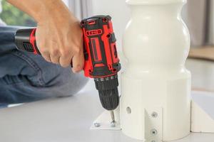 man assembling white table furniture at home using cordless screwdriver photo