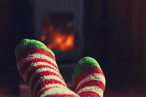 pies piernas en ropa de invierno calcetines de lana en el fondo de la chimenea. mujer sentada en casa en la noche de invierno u otoño relajándose y calentándose. concepto de invierno y clima frío. Nochebuena higiénica. foto