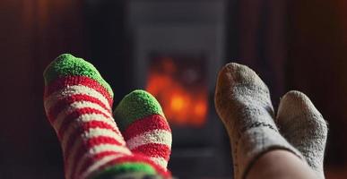 Two pair feet legs in winter wool socks at fireplace background. Couple family sitting at home on winter or autumn evening relaxing and warming up. Winter and cold weather concept, hygge Christmas eve photo