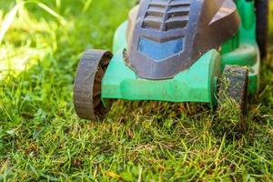 Lawn mower cutting green grass in backyard in sunny day. Gardening country lifestyle background. Beautiful view on fresh green grass lawn in sunlight, garden landscape in spring or summer season. photo