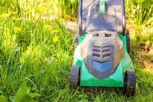 Lawn mower cutting green grass in backyard in sunny day. Gardening country lifestyle background. Beautiful view on fresh green grass lawn in sunlight, garden landscape in spring or summer season. photo