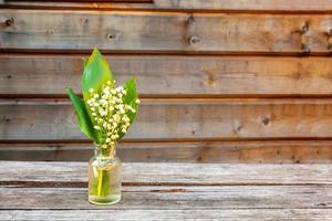 Bouquet of flowers smell lily of the valley or may-lily in glass vase on rustic old vintage wooden background. Garden in spring or summer concept. Close-up blossom twigs of Lilly of the valley. photo