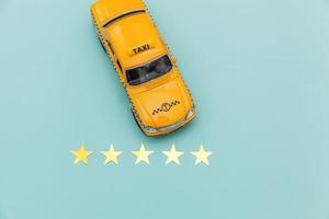 taxi de coche de juguete amarillo y calificación de 5 estrellas aislado sobre fondo azul. aplicación de teléfono inteligente del servicio de taxi para buscar en línea llamadas y reservar el concepto de taxi. símbolo de taxi. copie el espacio foto