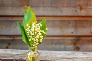 Bouquet of flowers beautiful smell lily of the valley or may-lily in glass vase on rustic old vintage wooden background. Garden in spring or summer concept. Close-up blossom twigs of Lilly of valley photo