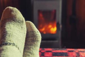 Feet legs in winter clothes wool socks at fireplace background. Woman sitting at home on winter or autumn evening relaxing and warming up. Winter and cold weather concept. Hygge Christmas eve. photo