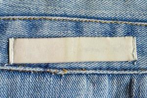 Blank white laundry care clothing label on denim jeans texture background photo