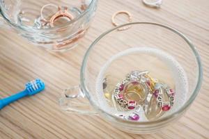 limpiar el anillo de diamantes de joyería con un vaso de agua caliente y líquido para lavar platos en el fondo de la mesa de madera foto