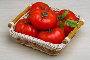 Red tomatoes in a basket on wooden background photo