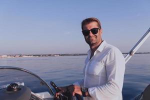 un hombre de negocios de alto nivel decidido con ropa informal y gafas de sol disfruta de sus vacaciones conduciendo un barco de lujo al atardecer. enfoque selectivo foto