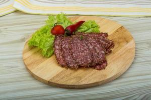 Sliced salami on wooden board and wooden background photo