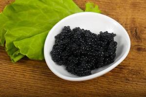 caviar negro en un recipiente sobre fondo de madera foto