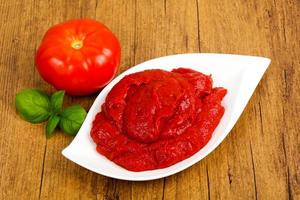 Tomato paste in a bowl on wooden background photo