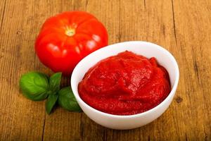 Tomato paste in a bowl on wooden background photo