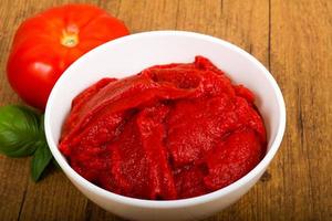 Tomato paste in a bowl on wooden background photo